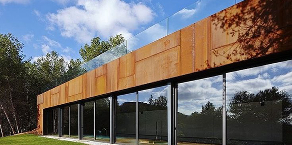 Villa contemporaine avec bardage supérieur en acier Corten et grandes baies vitrées donnant sur un environnement paysager.