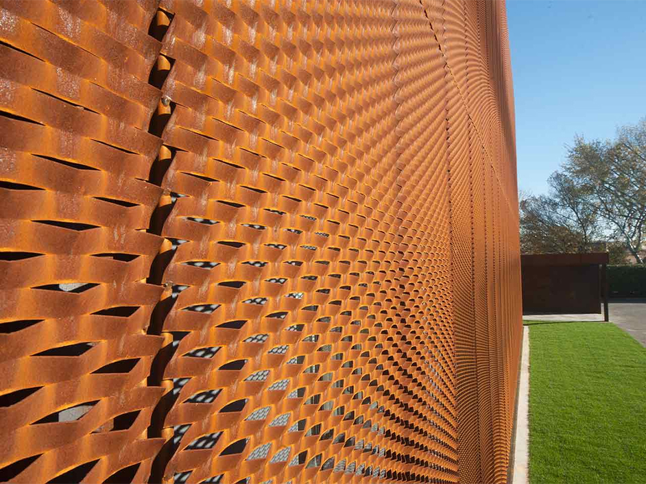 Détail d’une façade architecturale ajourée en acier Corten avec motif métallique tridimensionnel.