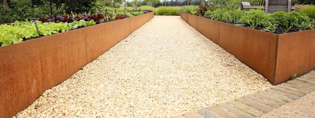 Bacs potagers surélevés en Acier Corten Maroc installés le long d’une allée en gravier dans un jardin cultivé.