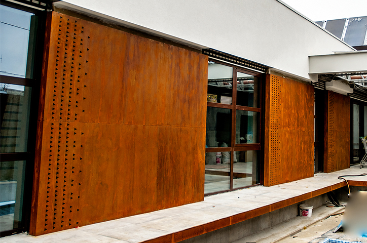 Façade contemporaine avec panneaux coulissants pleins et ajourés en acier Corten devant de grandes baies vitrées.