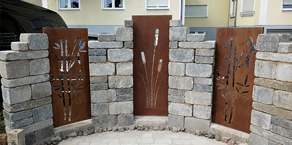 Panneaux décoratifs en acier Corten avec motifs végétaux ajourés intégrés entre des murs en pierre naturelle.
