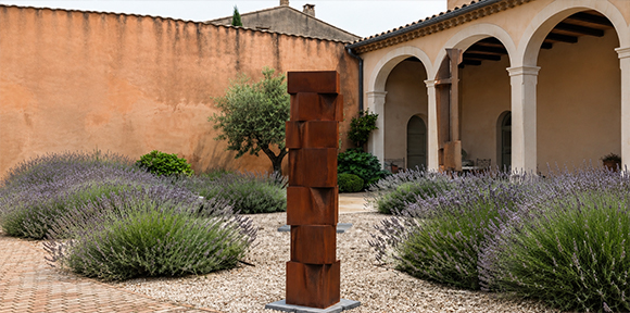 Sculpture verticale contemporaine réalisée dans le cadre de la Fabrication acier Corten et installée dans un jardin paysager.