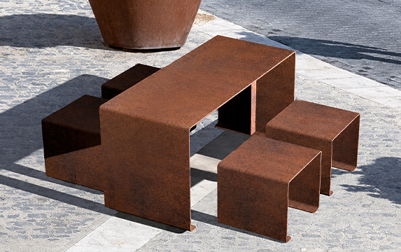 Mobilier extérieur en acier Corten avec table et tabourets sur une terrasse d’hôtel, parmi nos Réalisations en acier Corten.