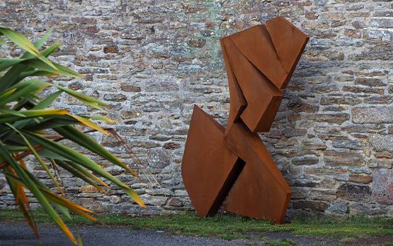 Sculpture abstraite installée dans le jardin d’une villa parmi nos Réalisations en acier Corten, devant un mur en pierre naturelle.